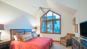 A bedroom with a large bed, a ceiling fan, a window, a TV, and a dresser.
