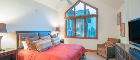 A bedroom with a large bed, a ceiling fan, a window, a TV, and a dresser.