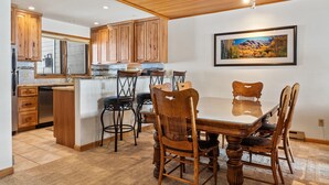 A kitchen with wooden cabinets, a dining table with chairs, and a large window. - Riverside Condos A103 by Avantstay Condo Close To Downtown, Town Park & Ski Lift #8 (Telluride)