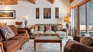 A cozy living room with a wooden ceiling, a brown leather sofa, a glass coffee table, and a large window. - Riverside Condos A103 by Avantstay Condo Close To Downtown, Town Park & Ski Lift #8 (Telluride)