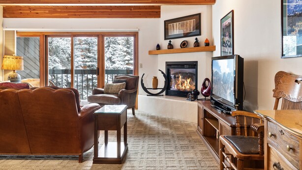 A cozy living room with a fireplace, wooden furniture, and a television. - Riverside Condos A103 by Avantstay Condo Close To Downtown, Town Park & Ski Lift #8 (Telluride)