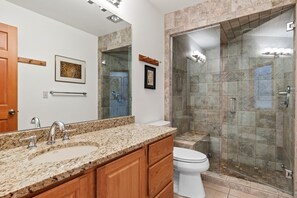 A bathroom with a granite countertop, a toilet, a shower with glass doors, and a wooden cabinet. - Riverside Condos A103 by Avantstay Condo Close To Downtown, Town Park & Ski Lift #8 (Telluride)