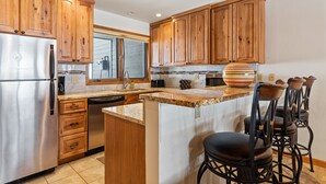 A kitchen with wooden cabinets, a stainless steel refrigerator, a dishwasher, and a marble countertop. - Riverside Condos A103 by Avantstay Condo Close To Downtown, Town Park & Ski Lift #8 (Telluride)