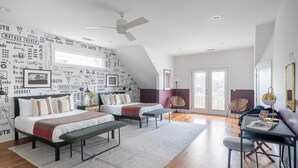 Une chambre moderne avec un plafond en pente, un ventilateur de plafond, un lit avec une banquette, un bureau avec une chaise et une grande fenêtre.