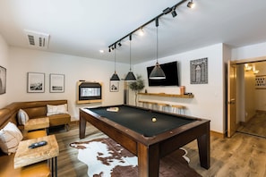 Ett vardagsrum med ett biljardbord, en soffa, en tv och inramade tavlor på väggen.