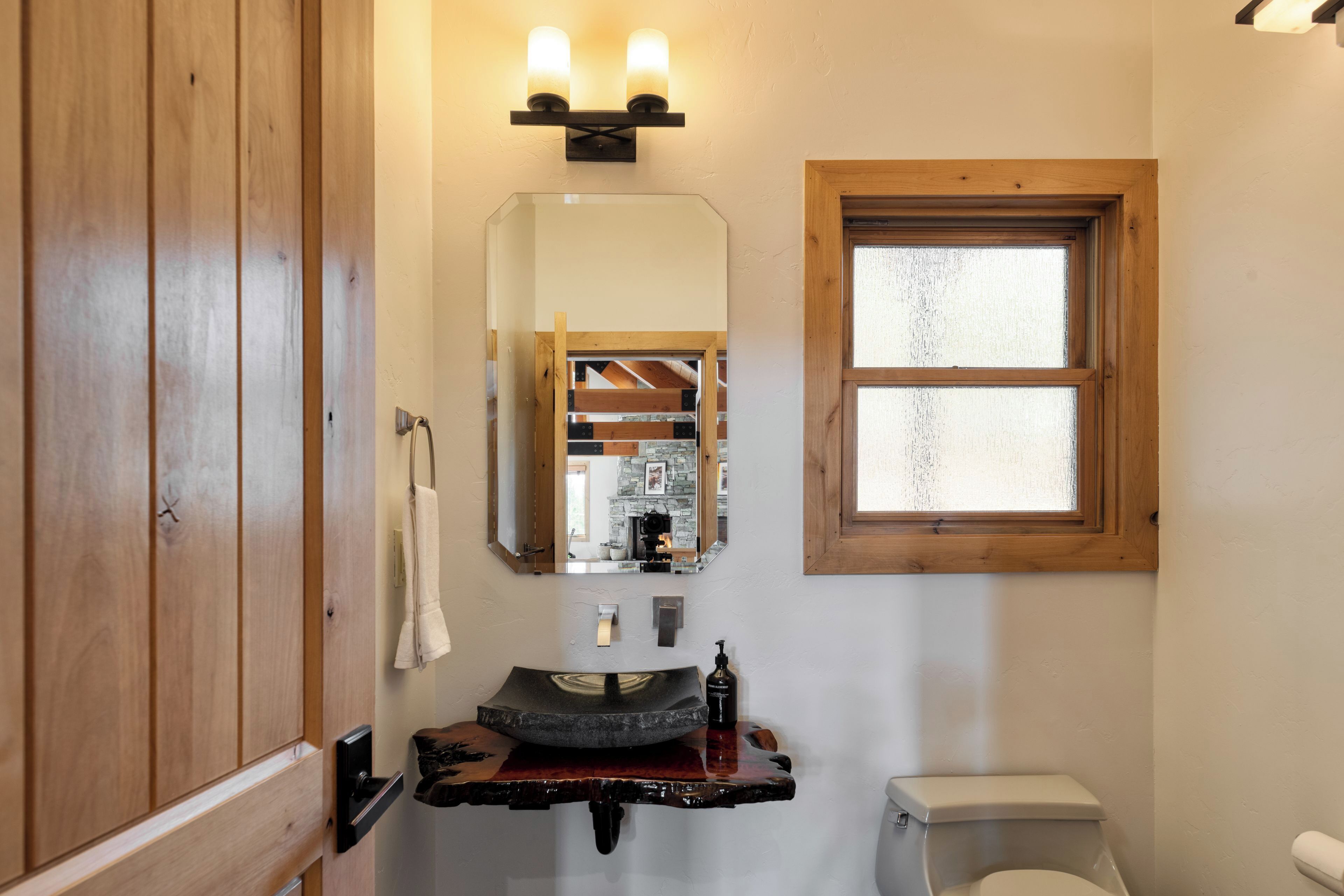 A bathroom with a wooden vanity, a large mirror, a window, and a sink with a soap dispenser.