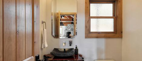 A bathroom with a wooden vanity, a large mirror, a window, and a sink with a soap dispenser.
