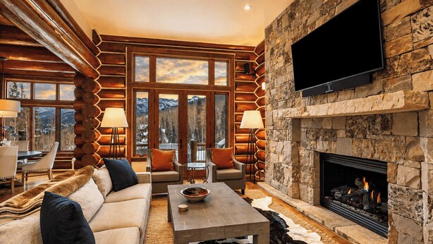 A log cabin interior with a stone fireplace, a flat-screen TV, and a cozy seating area.