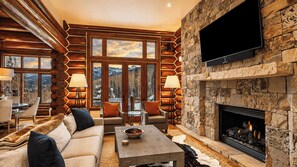 A log cabin interior with a stone fireplace, a flat-screen TV, and a cozy seating area.