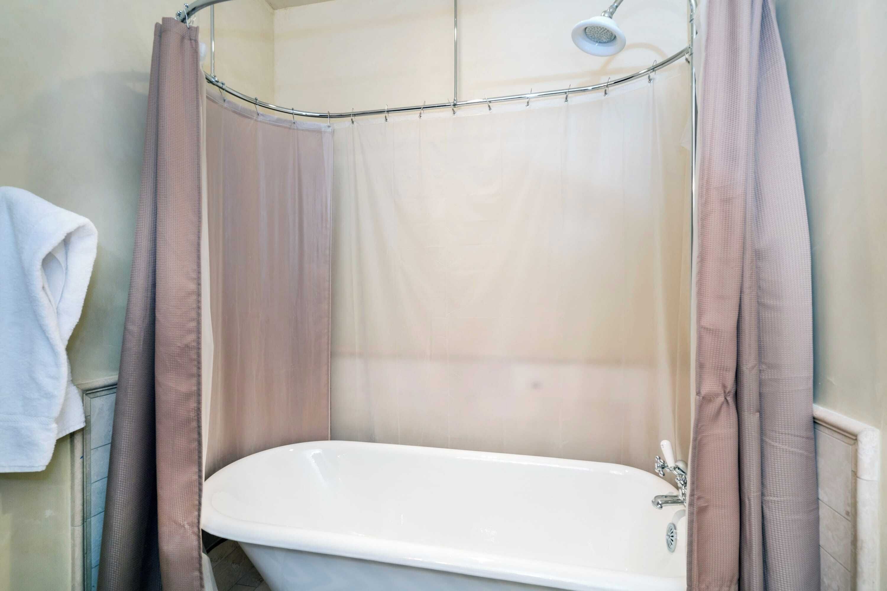 A bathroom with a bathtub, shower curtain, and a towel hanging on the wall.