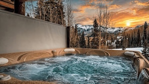 A hot tub with a mountainous backdrop, surrounded by trees and a clear sky.