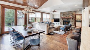 A spacious living area with a wooden ceiling, a stone fireplace, and a large window overlooking a backyard. - Modern 5bdr Right off Main Street w/ Hot Tub Main Street Escape by Avantstay (Park City)