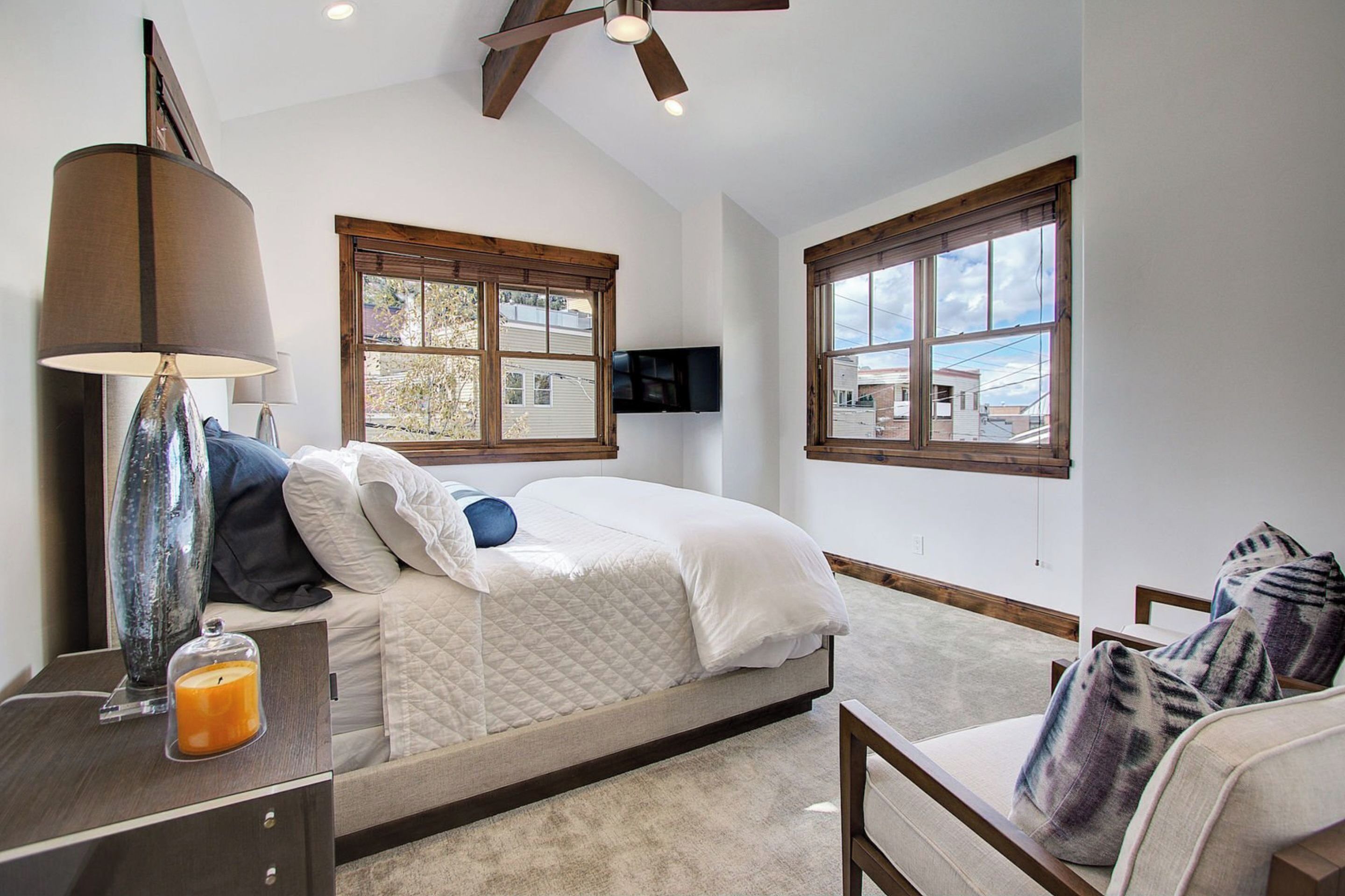A bedroom with a bed, a nightstand with a lamp, a TV, and a window.