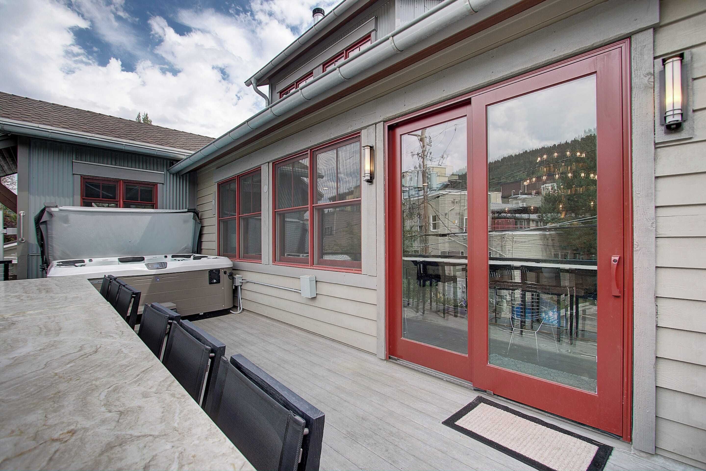 An outdoor deck with a table and chairs, a hot tub, and a sliding glass door with a red frame.