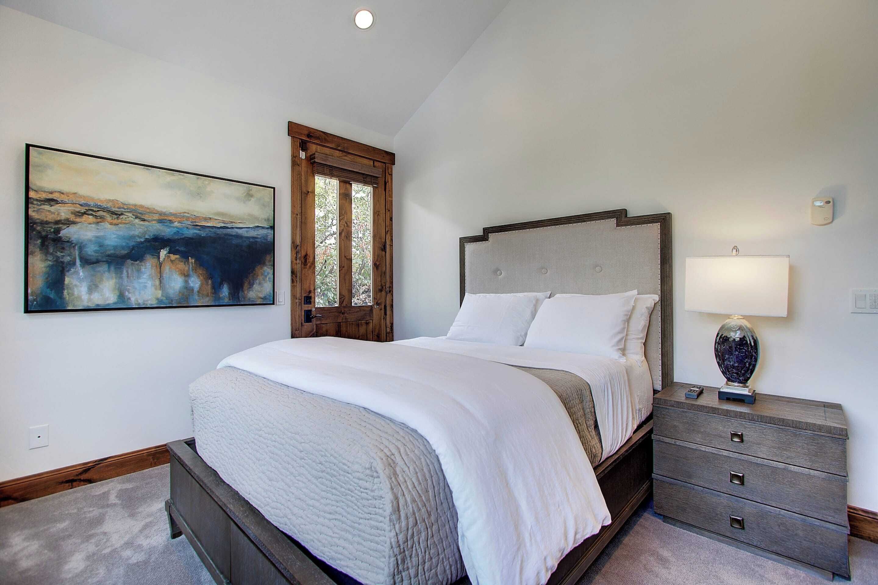 A bedroom with a large bed, a nightstand, a lamp, and a painting on the wall.