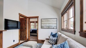 A living room with a large window, a flat-screen TV, a sofa with cushions, and a wooden door leading to another room. - Modern 5bdr Right off Main Street w/ Hot Tub Main Street Escape by Avantstay (Park City)