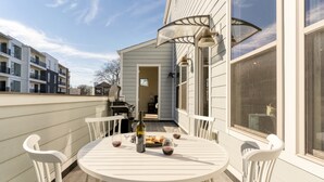 A round white table with chairs on a wooden deck, a bottle, and glasses of red wine.