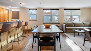 Une cuisine moderne avec un îlot central en bois et des tabourets de bar, un coin repas avec une grande table et des chaises, et un espace salon confortable avec un canapé et une table basse.