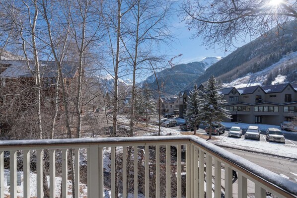 A snow-covered balcony with a view of a mountain range, a parking lot with cars, and buildings in the background. - Plunge A by Avantstay Stunning Views & A Block From Lift #7 (Telluride)