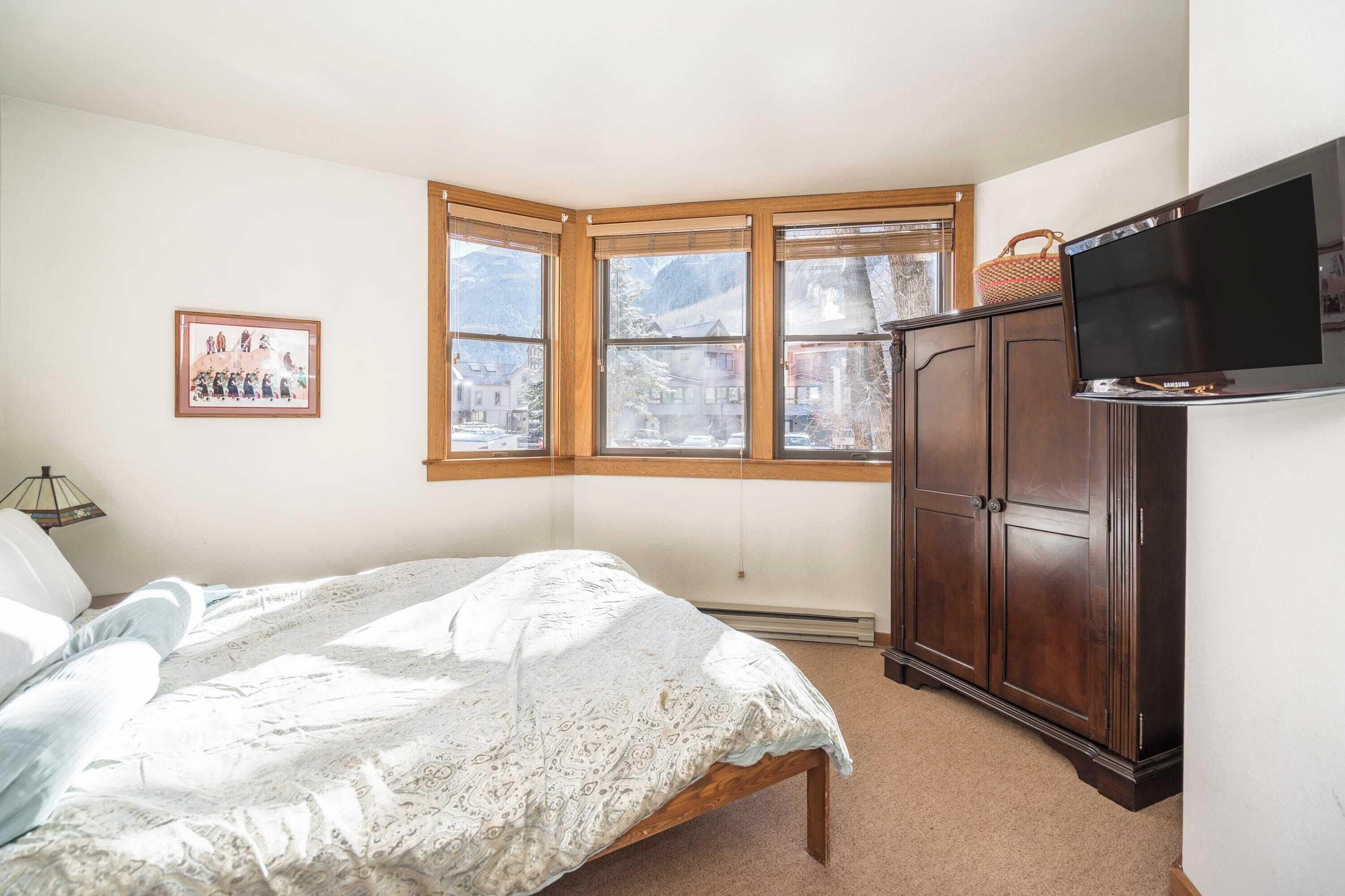 Un dormitorio con cama, armario de madera, televisión y ventana con vistas a las montañas.