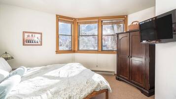 Un dormitorio con cama, armario de madera, televisión y ventana con vistas a las montañas.
