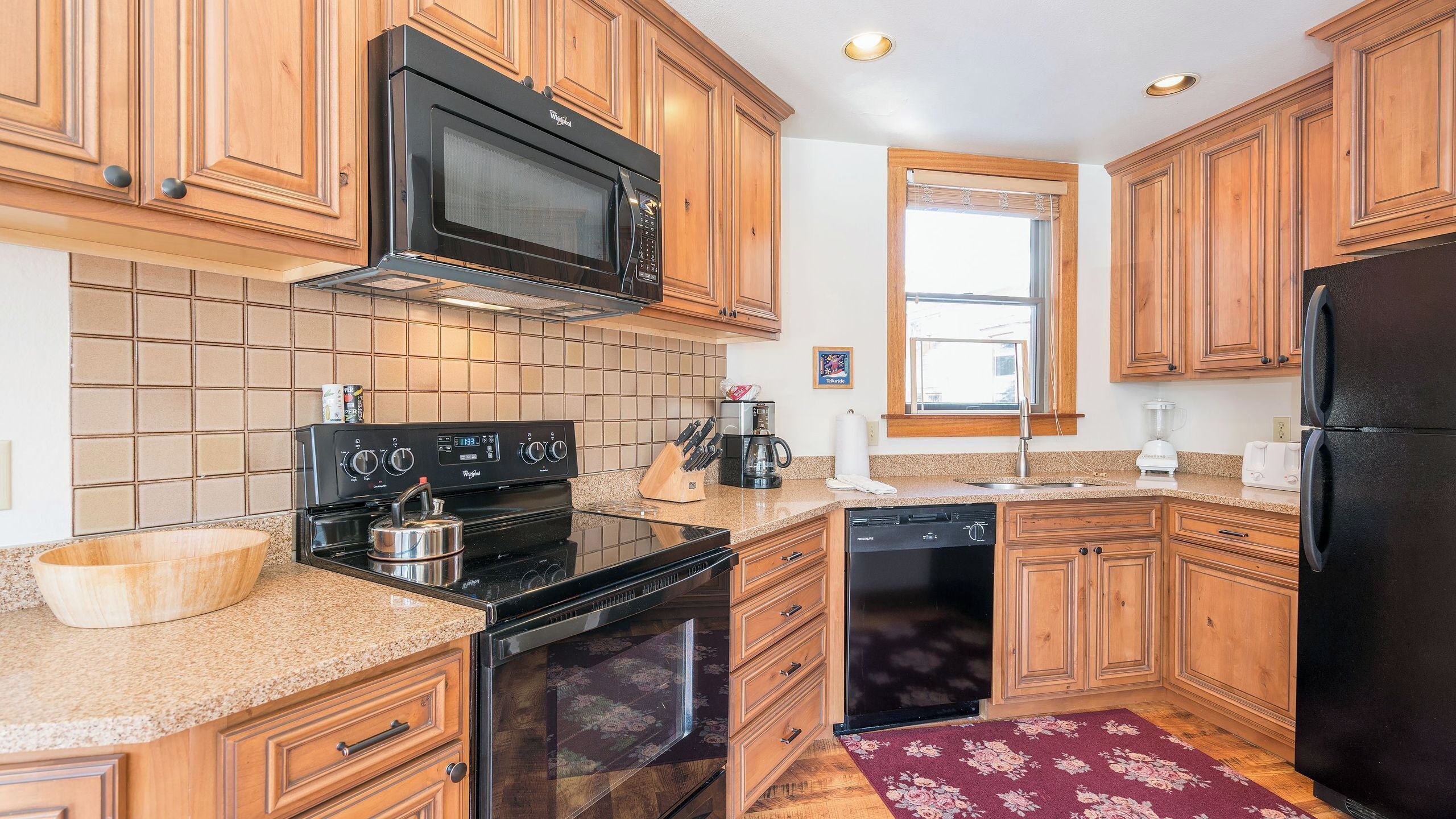 A kitchen with wooden cabinets, a black microwave, a stove, a dishwasher, and a refrigerator.