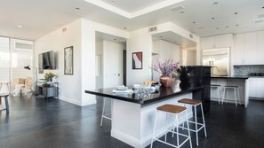 A modern kitchen with a black countertop, white bar stools, and a large island. - Balboa I by Avantstay - Stylish Condo Balboa Park Adjacent w/ Views! (San Diego)