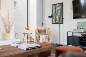 A modern living room with a wooden coffee table, books, a wicker chair, a floor lamp, and a television on a black stand. - Balboa I by Avantstay - Stylish Condo Balboa Park Adjacent w/ Views! (San Diego)