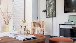 A modern living room with a wooden coffee table, books, a wicker chair, a floor lamp, and a television. - Balboa I by Avantstay - Stylish Condo Balboa Park Adjacent w/ Views! (San Diego)