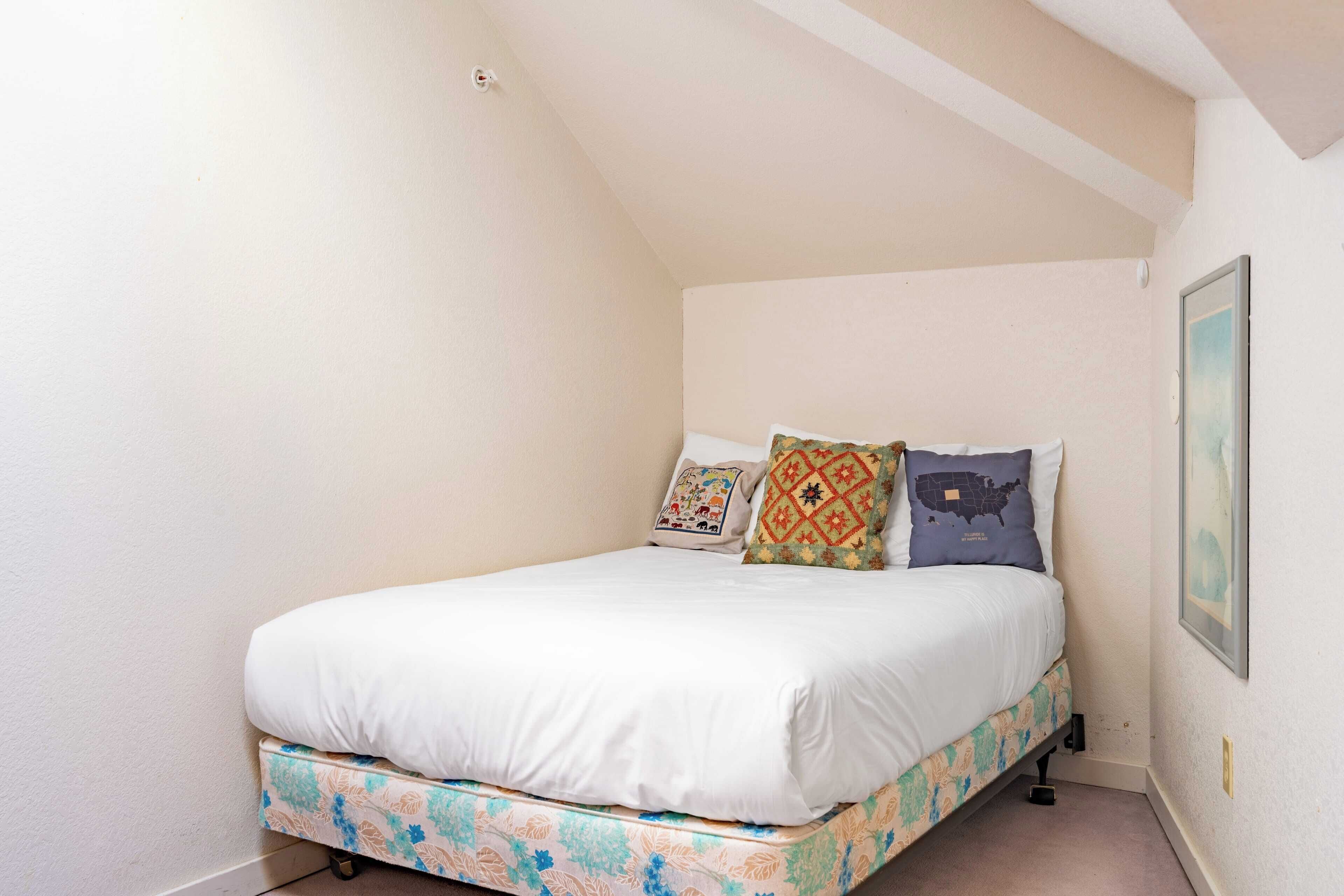 A single bed with patterned bedding, a wall-mounted light, and a framed picture on the wall.