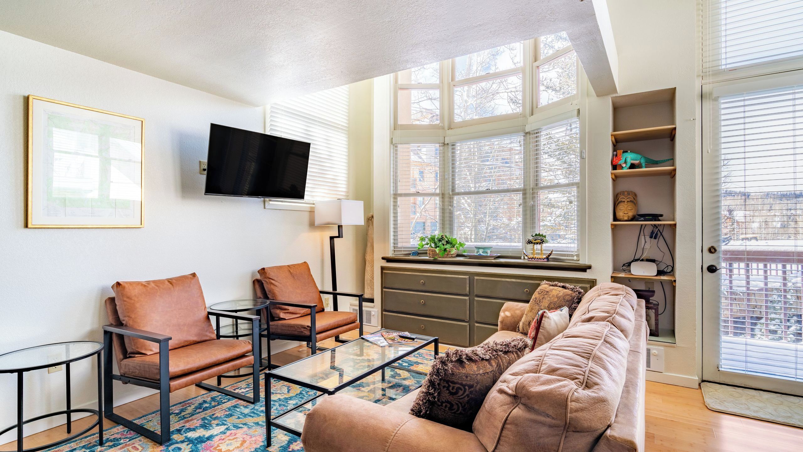 A living room with a sofa, chairs, a coffee table, a TV, and a window with blinds.