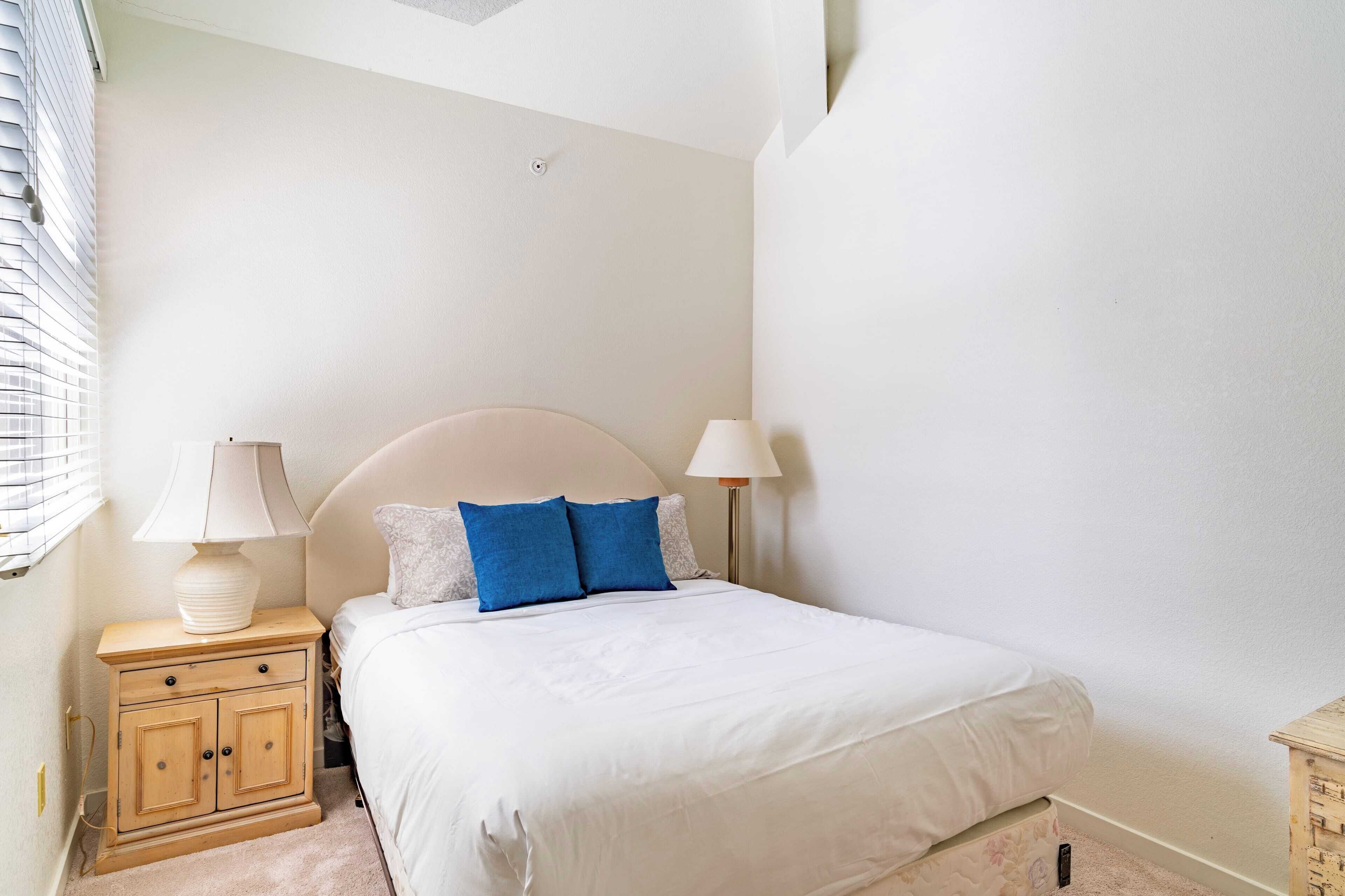 Quarto com cama, duas luminárias de cabeceira, mesa de cabeceira e um pequeno armário de madeira.