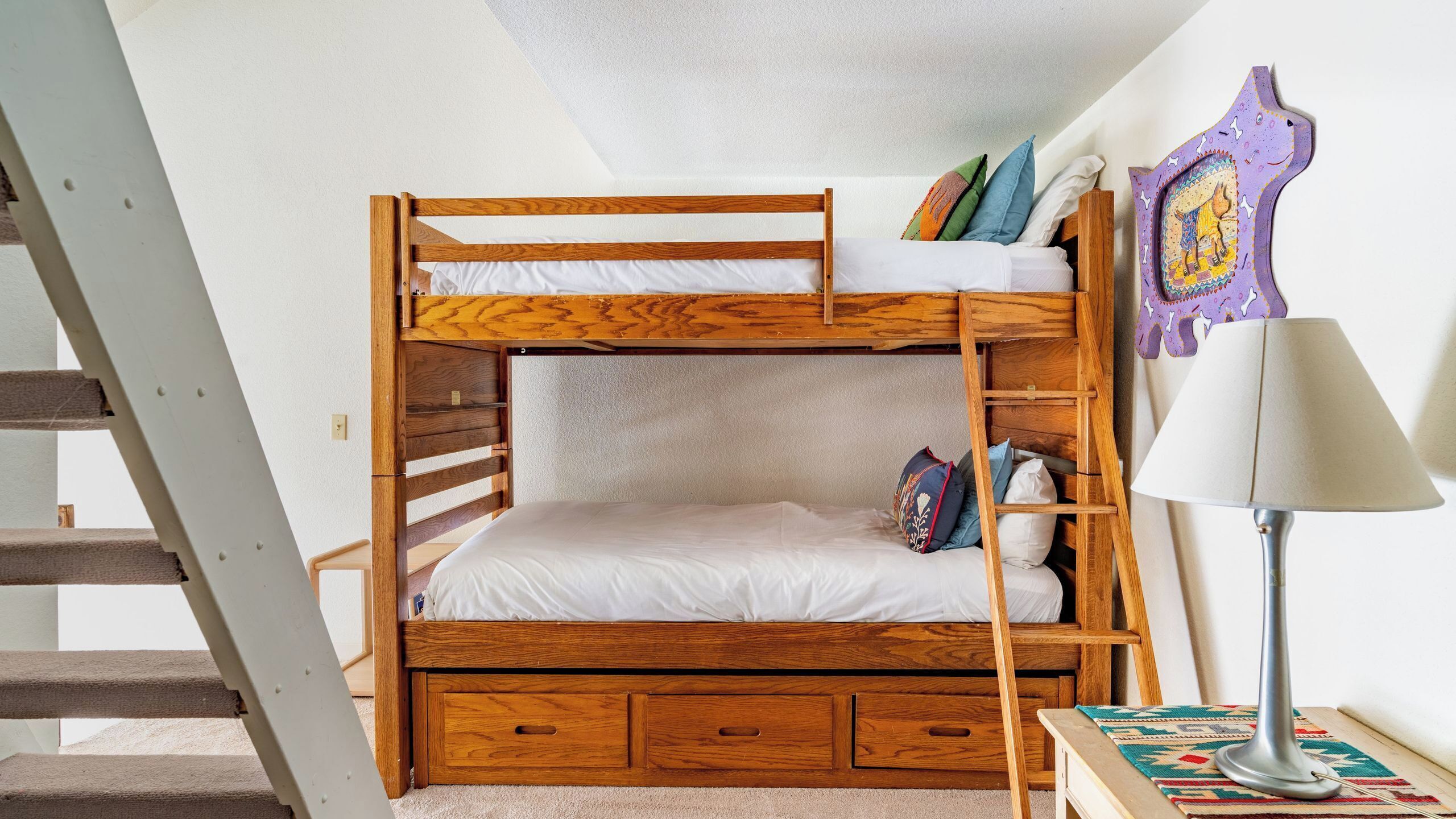 A bunk bed with a wooden frame, a small desk, a lamp, and a colorful wall hanging.
