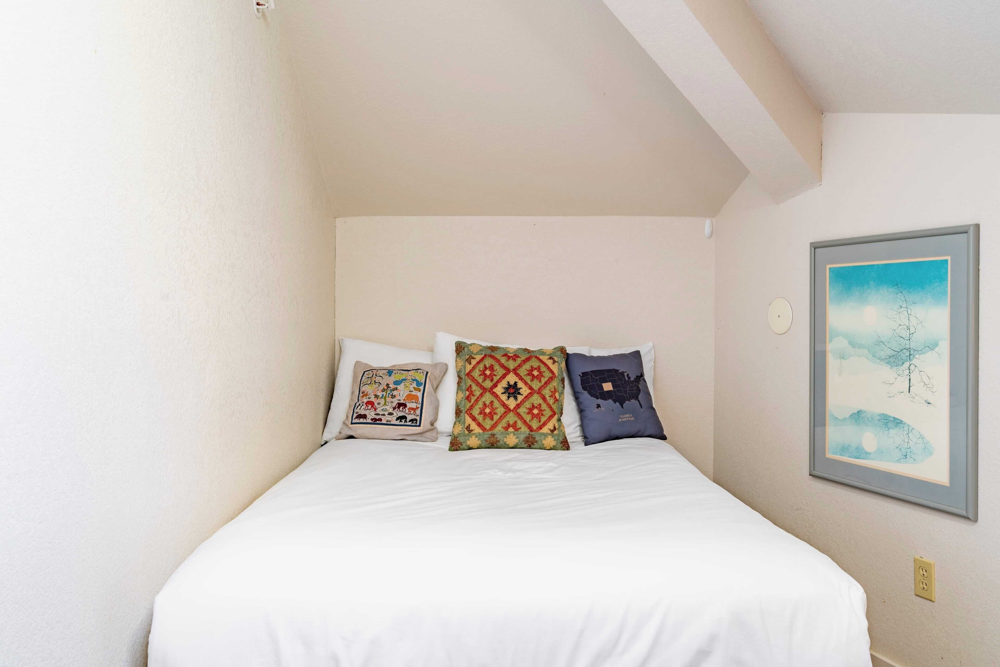 Un dormitorio con una cama, tres almohadas y un cuadro enmarcado en la pared.