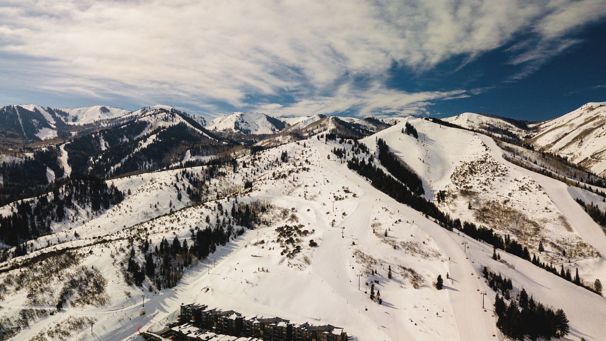 A snow-covered mountain landscape with ski slopes, ski lifts, and a cluster of buildings at the base.