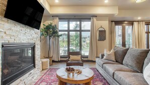 A living room with a fireplace, a sofa, a coffee table with pinecones, and large windows with curtains. - Kestrel by Avantstay Close to the Ski Slopes in This Majestic Home in Park City (Park City)