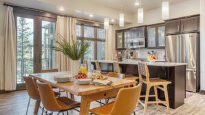 A modern kitchen with dark cabinets, stainless steel appliances, and a wooden dining table with chairs. - Kestrel by Avantstay Close to the Ski Slopes in This Majestic Home in Park City (Park City)