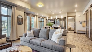 A modern living room with a grey sofa, a wooden coffee table, and a view of the kitchen.