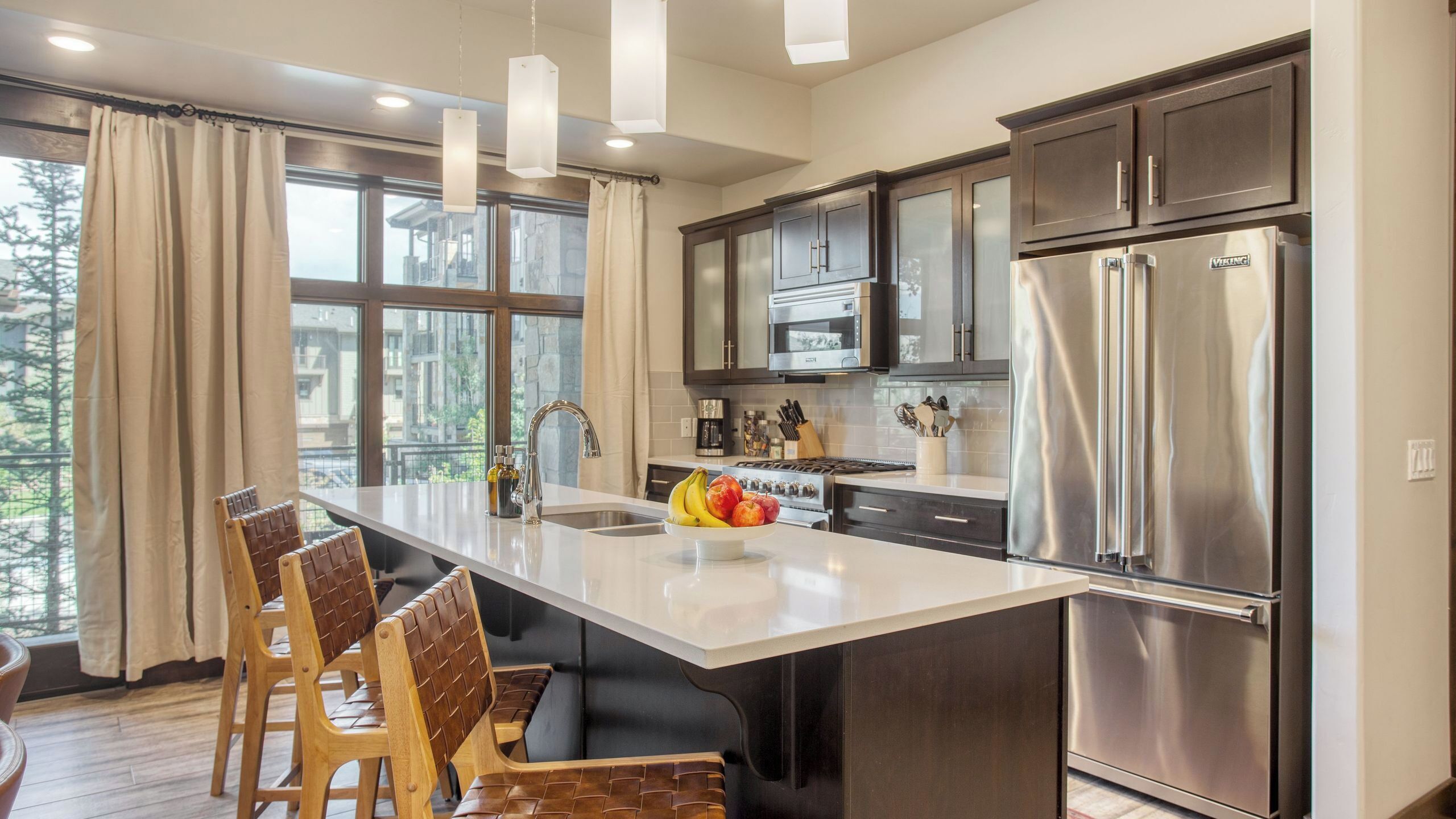 A modern kitchen with a central island, stainless steel appliances, and a view of the outdoors.