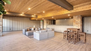 A spacious living area with a wooden ceiling, a stone accent wall, a gray sectional sofa, and a wooden dining set.