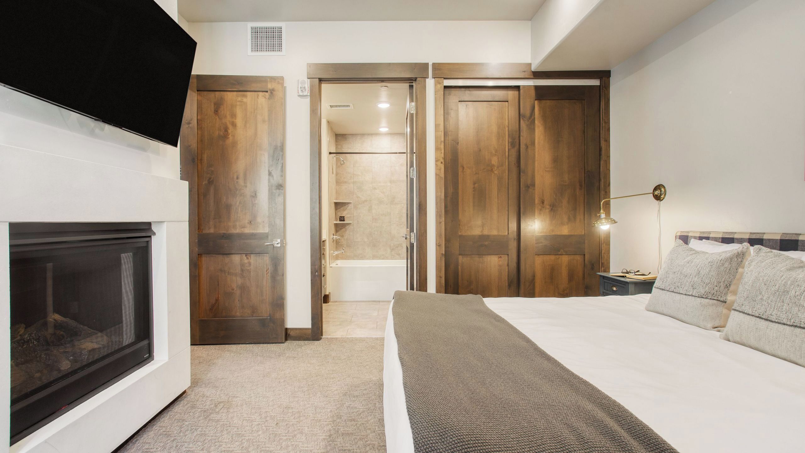 A bedroom with a bed, bedside table, lamp, and a view into the bathroom.