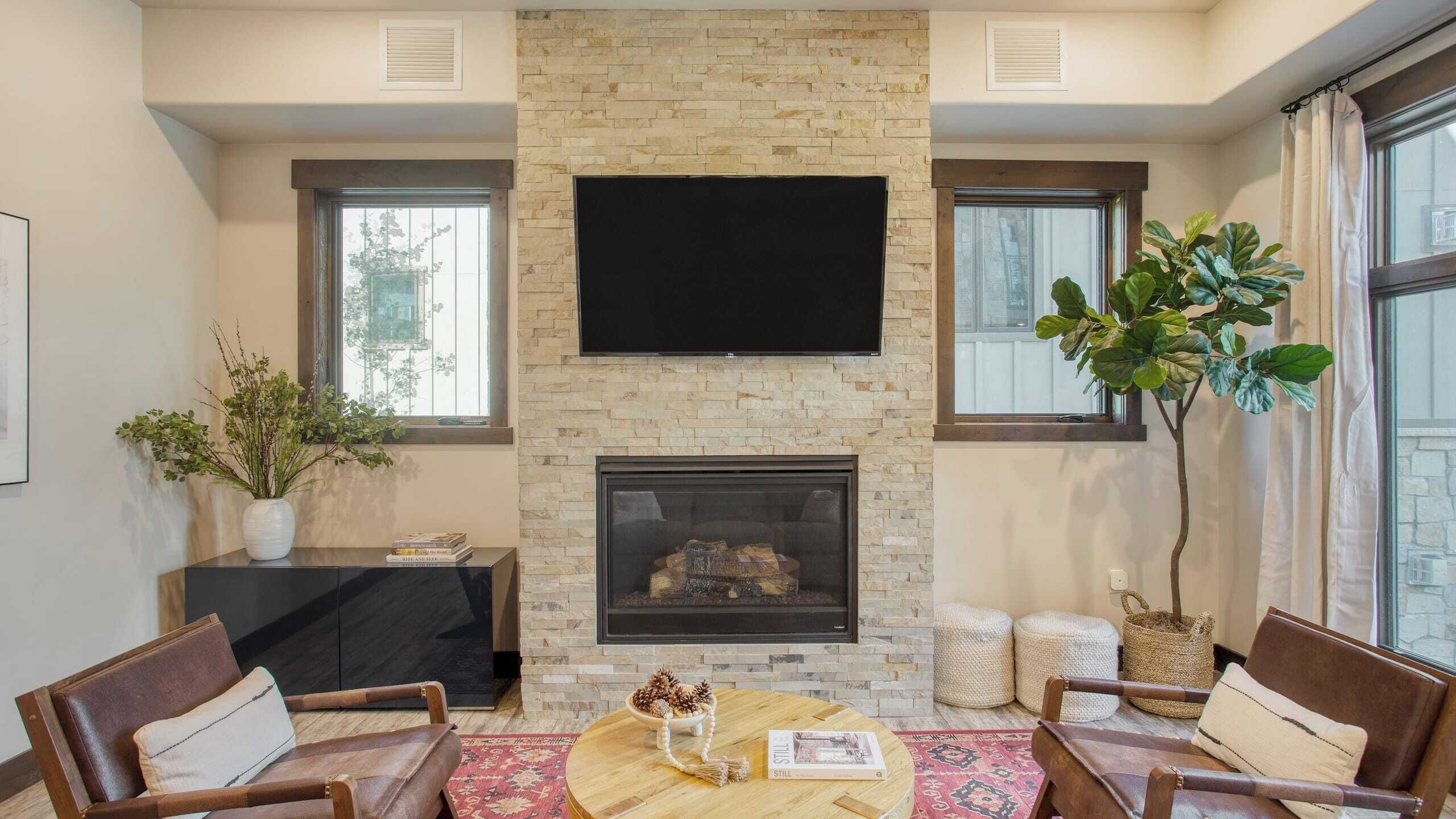 A living room with a stone fireplace, a flat-screen TV mounted above it, and a large window on one side.