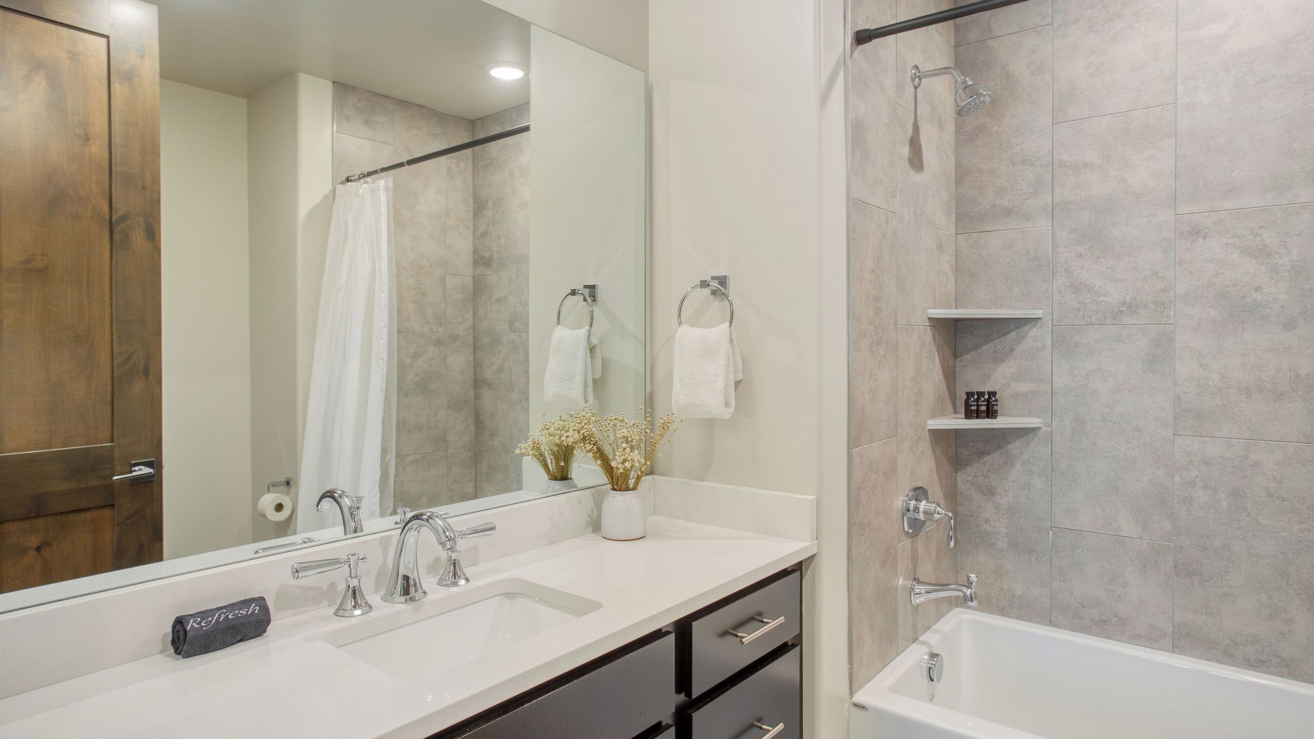 A modern bathroom with a large mirror, two sinks, a shower, and a bathtub.