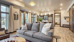 A modern living room with a grey sofa, wooden coffee table, and a view of the kitchen and dining area. - Kestrel by Avantstay Close to the Ski Slopes in This Majestic Home in Park City (Park City)