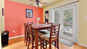 Un coin repas avec une table et des chaises en bois, un ventilateur de plafond et une porte donnant sur un balcon.