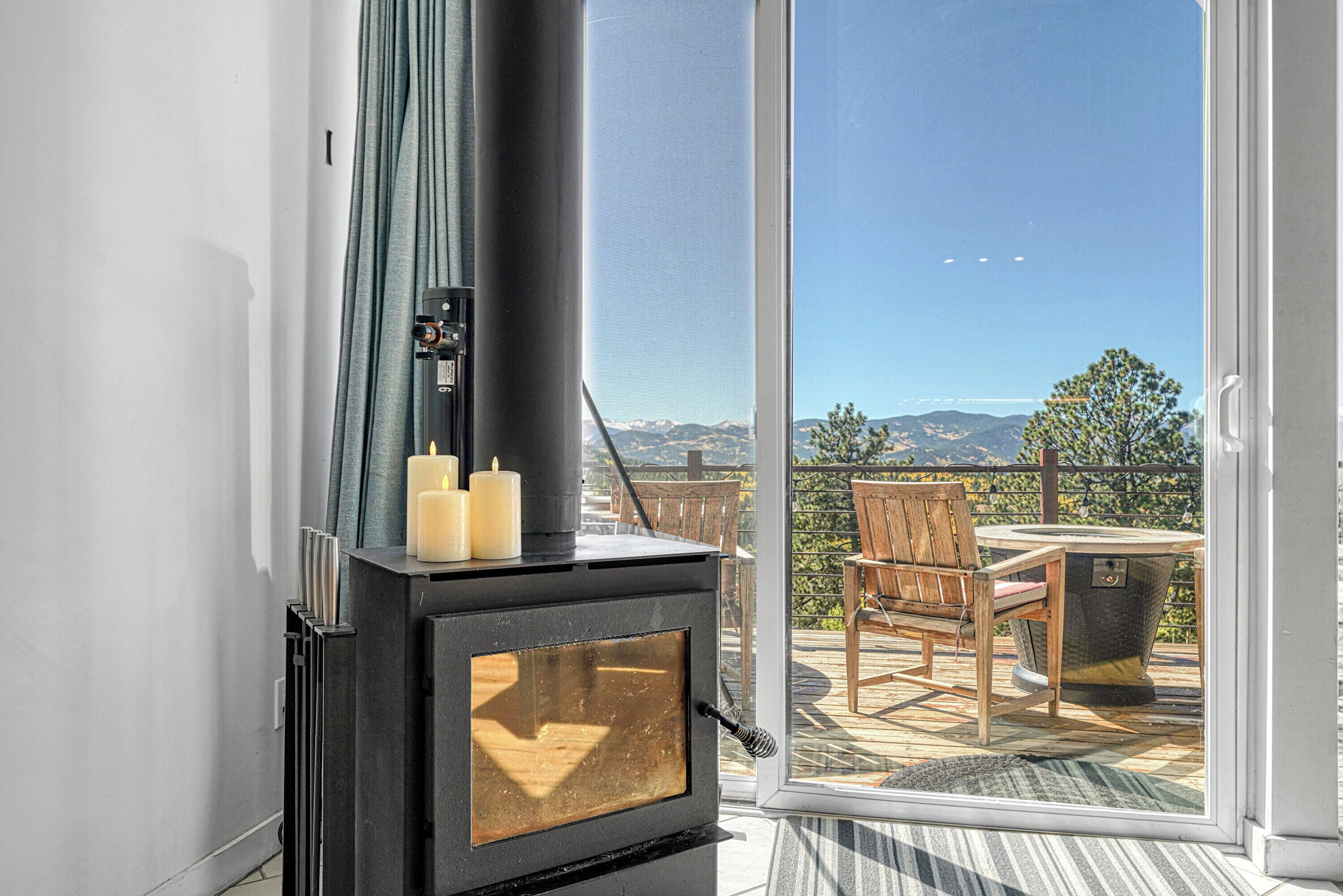 A modern room with a wood-burning stove, a glass door leading to an outdoor patio with a table and chairs, and a view of mountains.