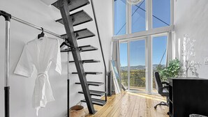 A room with a wooden floor, a black office chair, a desk, a white robe hanging on a rack, a ladder, and a large window with a view of the outdoors. - Off-grid Masterpiece Cabin W/ Breathtaking View (Central City)