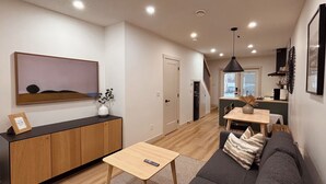 A modern living room with a sofa, a coffee table, and a TV on a wooden cabinet. There is a staircase leading to a kitchen area. - The overlook stay  Free parking 35 (Harvie Heights)