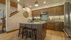 A modern kitchen with wooden cabinets, a stainless steel refrigerator, and a central island with bar stools. - Sawtooth by Avantstay Spacious Pine Tree Cabin w/ Hot Tub (Truckee)