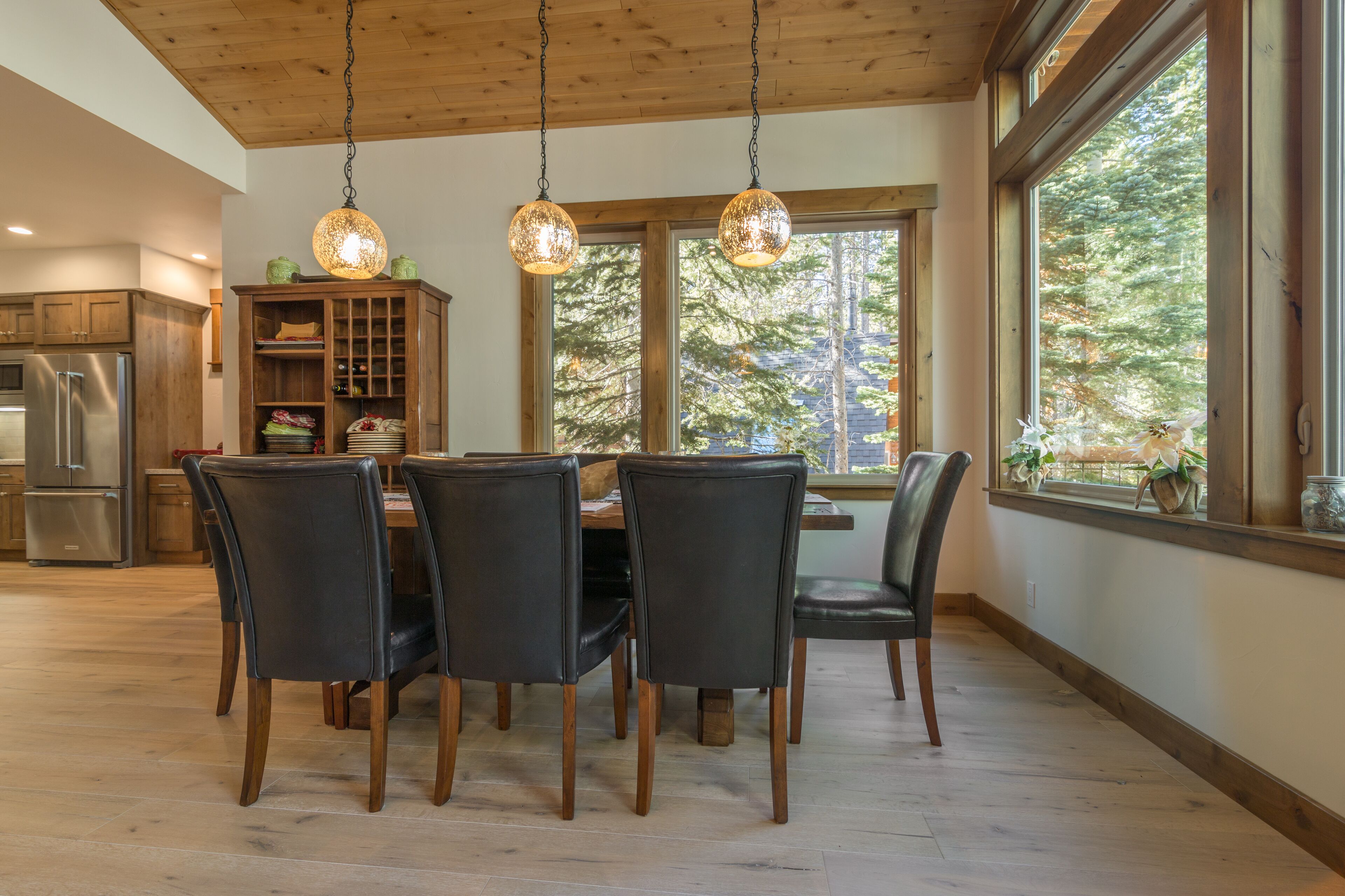 Een eetruimte met een houten tafel en stoelen, een inbouwkast en een groot raam met uitzicht op bomen.